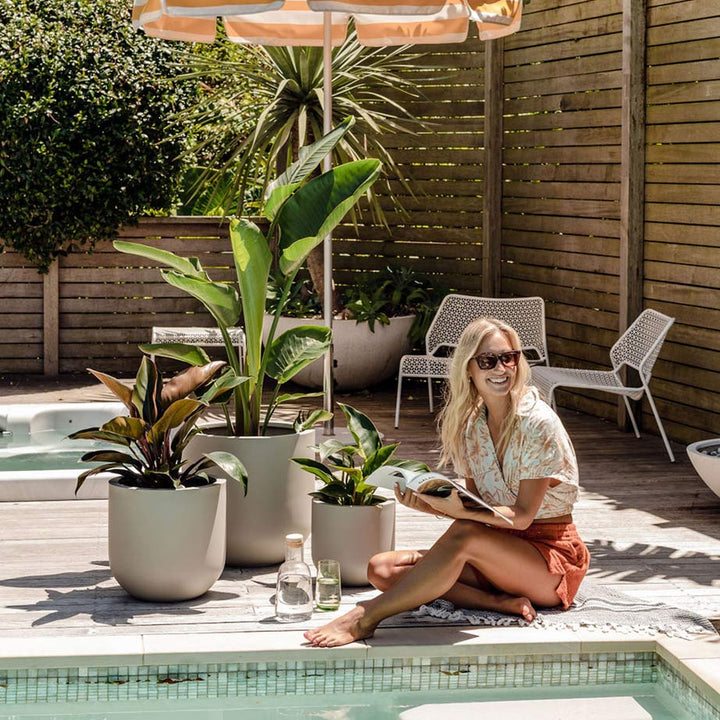 A happy plant enthusiast relaxes beside her Thomas garden pots while reading a design magazine in the sunshine.
