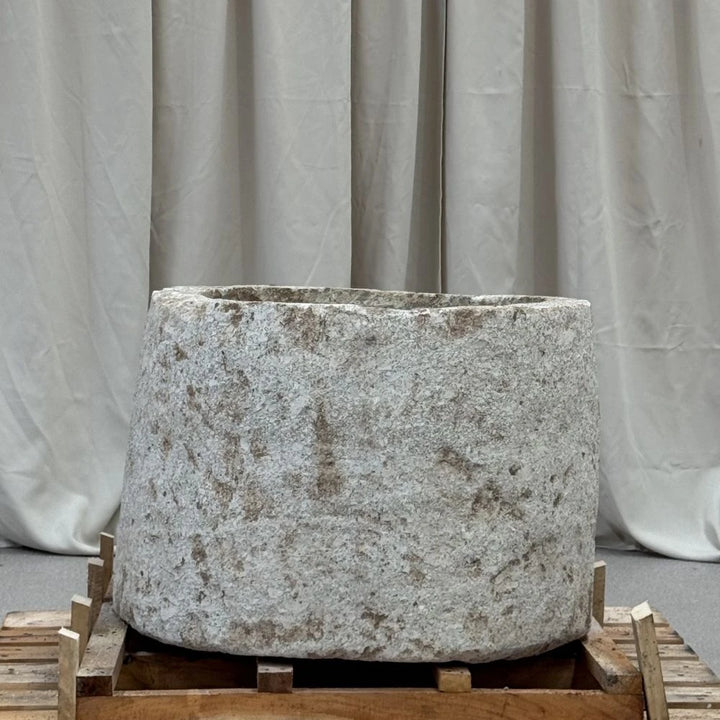Large stone planter on a wooden pallet with a gray curtain background
