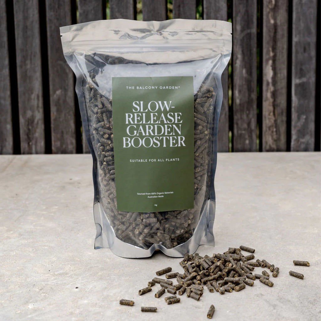 The Balcony Garden Slow Release Garden Booster bag on a rustic table, with organic fertilizer pellets scattered in front, perfect for sustainable gardening
